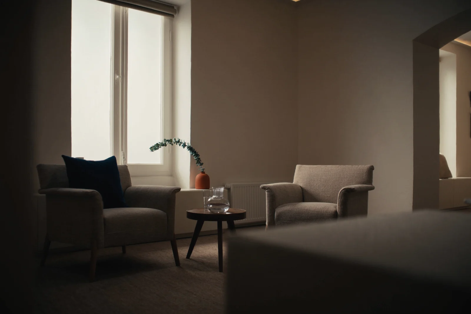 Two armchairs either side of a small walnut table with a carafe of water, by a tall window
