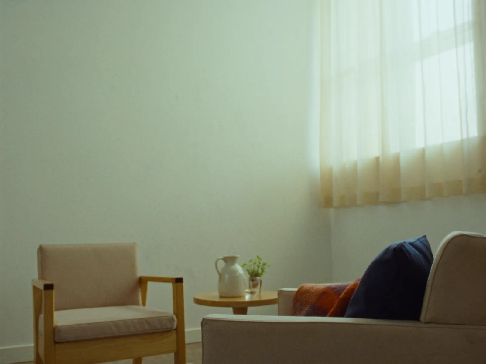 An empty therapy room in soft daylight, two armchairs and a small table by a sheer-curtained window